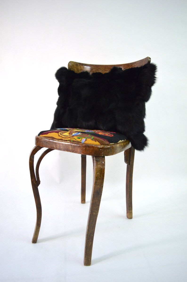 May include: A black faux fur pillow sits on a wooden chair with a colorful floral patterned seat. The chair has a curved back and four legs.
