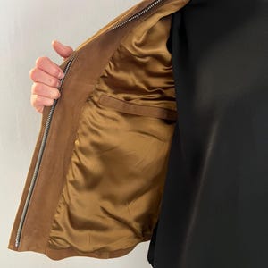 May include: A brown suede jacket with a zip fastening. The interior lining is a golden-brown satin. The jacket has a classic design and a tailored fit, suitable for various occasions.