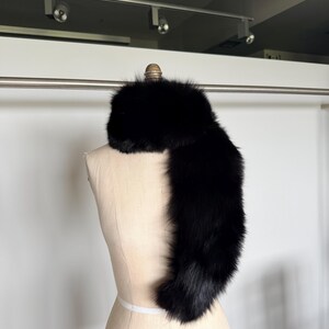 May include: A luxurious black fur scarf draped over a mannequin. The scarf is made of soft, dense fur, and it is a deep, solid black color. The mannequin is a light beige color, and the background is a plain white wall.