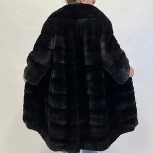 May include: A black fur coat with a long, flowing silhouette. The coat is made of soft, luxurious fur and has a classic, elegant design.