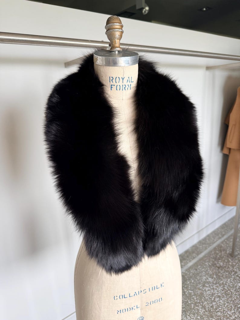 May include: A luxurious black fur collar displayed on a mannequin. The collar is thick and plush, with a deep, rich black color. The mannequin is a neutral beige color, and the background is a bright white.