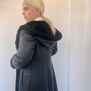 Echtpelz-Mantel aus schwarzem Nappamontur mit Kapuze in A-Linie. Echte dicke Lammfelljacke. Echter Schaffell Pelzmantel, Luxus Pelz Geschenk