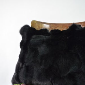 May include: A black faux fur pillow resting on a colorful floral patterned fabric.