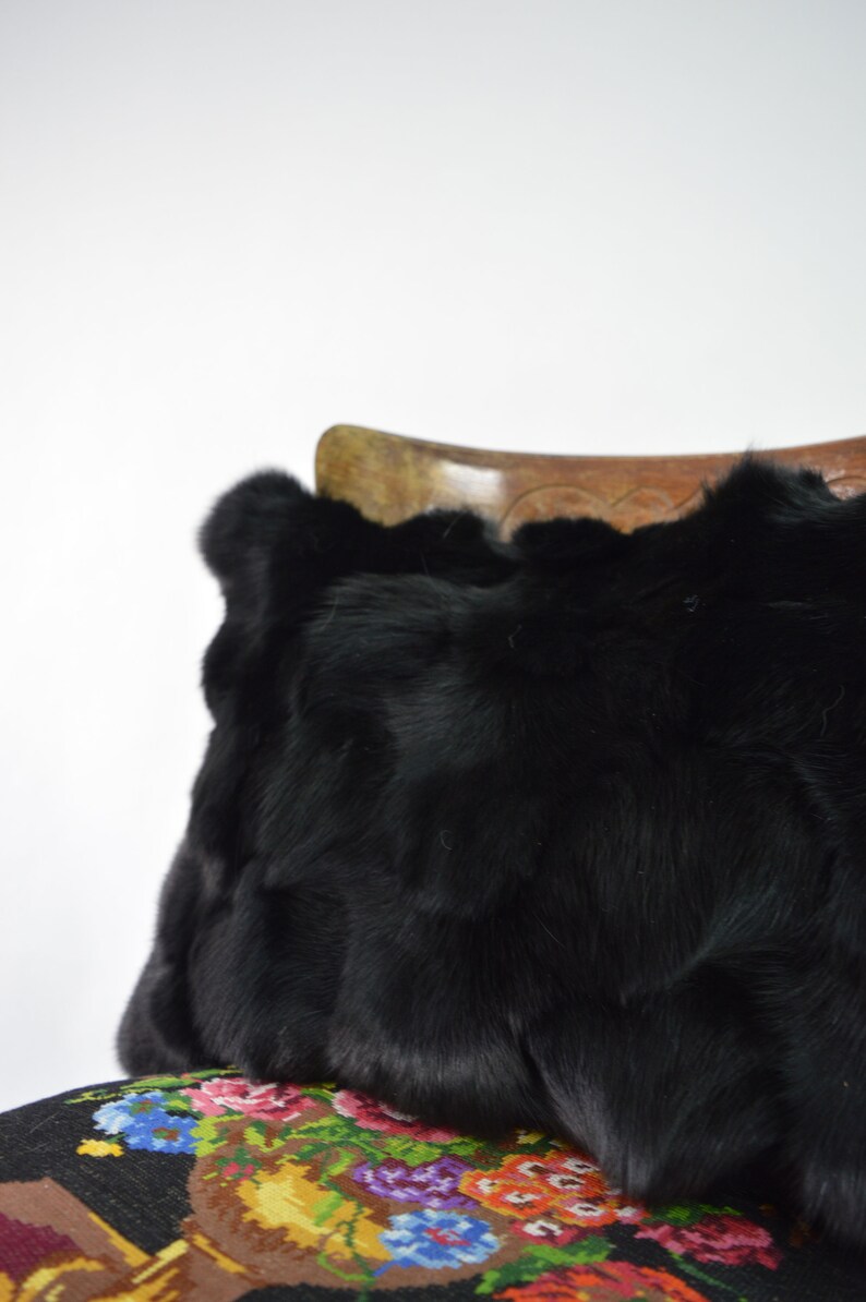 May include: A black faux fur pillow resting on a colorful floral patterned fabric.
