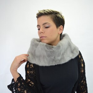May include: A woman wearing a grey fur collar over a black crochet top.