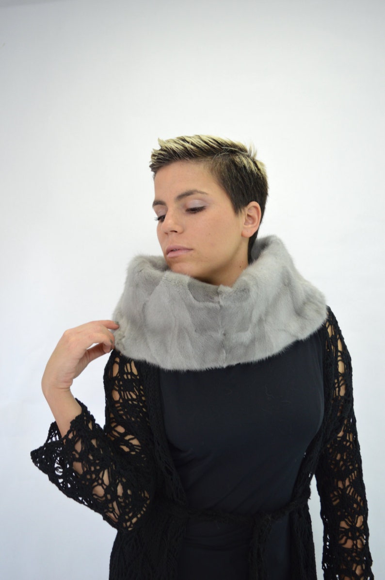 May include: A woman wearing a grey fur collar over a black crochet top.