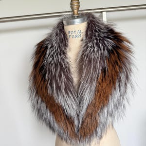 May include: A luxurious fur collar with a mix of brown, silver, and orange tones. The collar is displayed on a mannequin, showcasing its shape and texture. The fur appears soft and fluffy, perfect for adding a touch of elegance to any outfit.