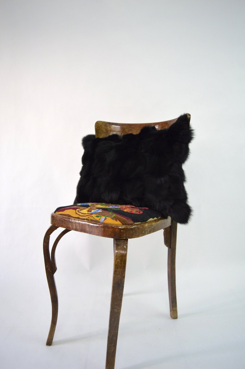 May include: A black faux fur pillow sits on a wooden chair with a colorful floral patterned seat. The chair has curved legs and a simple design.