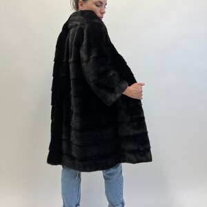 May include: A long black fur coat with a collar. The coat is made of mink fur and has a sleek, elegant design.