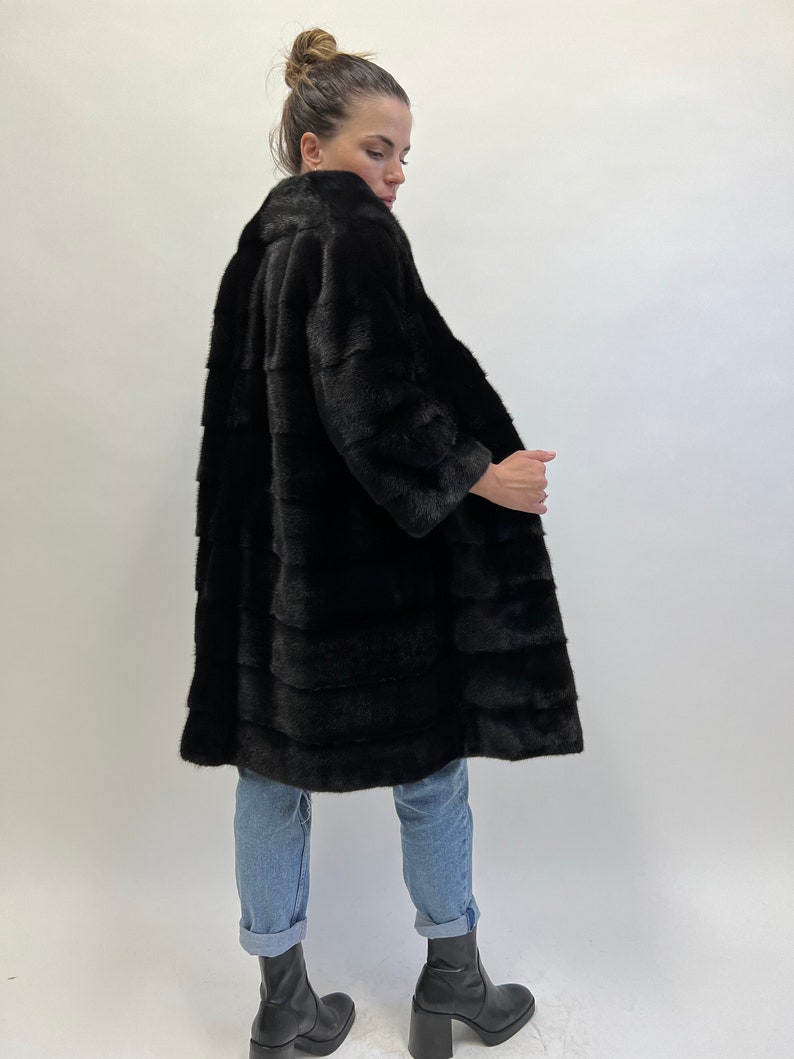 May include: A long black fur coat with a collar. The coat is made of mink fur and has a sleek, elegant design.