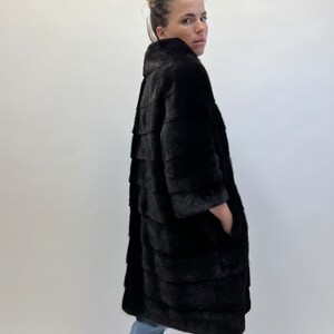 May include: A black fur coat with a long, straight silhouette and a high collar. The coat has a smooth, sleek texture and is made of high-quality fur.