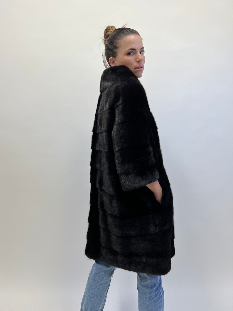 May include: A black fur coat with a long, straight silhouette and a high collar. The coat has a smooth, sleek texture and is made of high-quality fur.