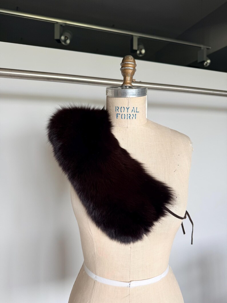 May include: A dark brown fur collar displayed on a vintage dress form. The collar is a rich, deep shade, with a soft, textured appearance. The dress form has the text "ROYAL FORM" printed on it.