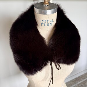 May include: A dark brown fur collar with a tie closure, displayed on a vintage dress form. The collar is plush and appears to be made of luxurious fur. The dress form has the text "ROYAL FORM" printed on it.