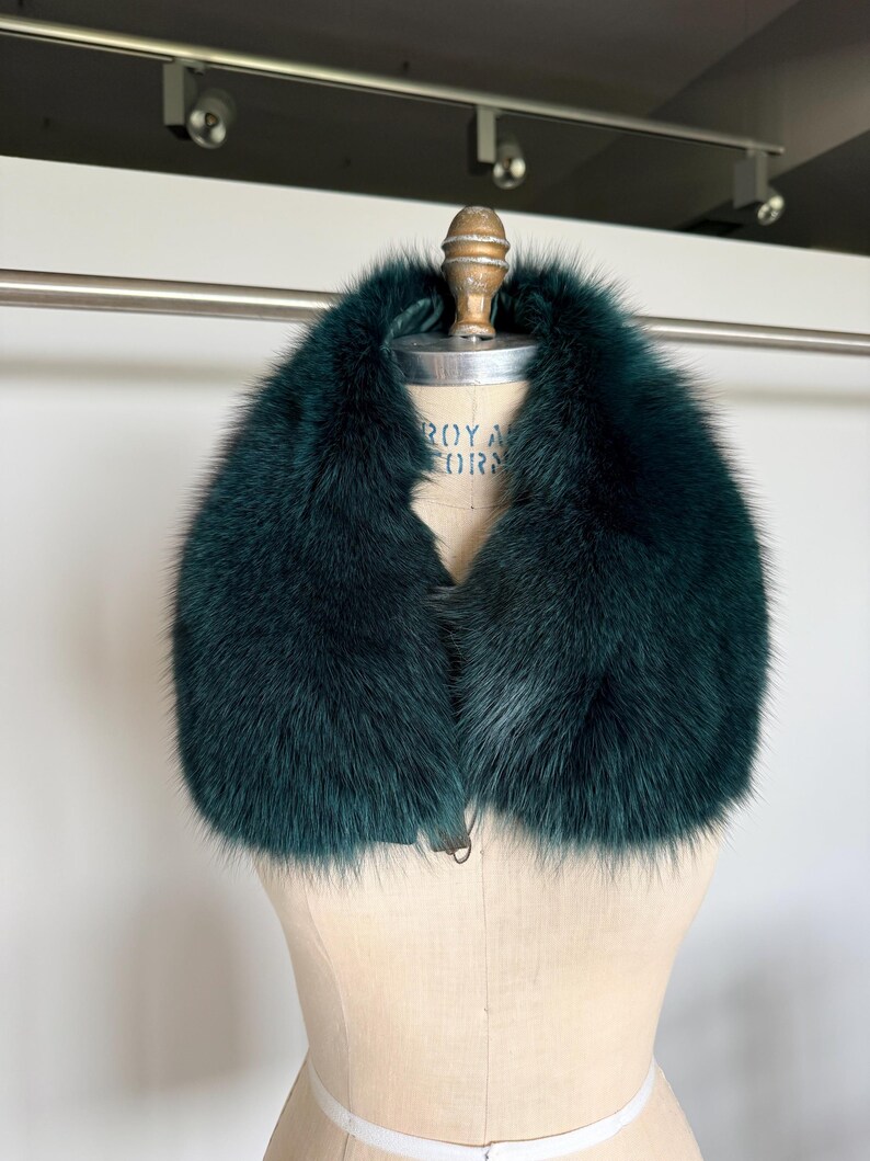 K&ouml;nnte beinhalten: Ein luxuri&ouml;ser, dunkelblauer Pelzkragen. Der Kragen wird auf einer Vintage-Schneiderpuppe pr&auml;sentiert. Das Fell wirkt weich und pl&uuml;schig, mit einer tiefen, satten Farbe. Der Kragen ist zum Tragen um den Hals konzipiert.
