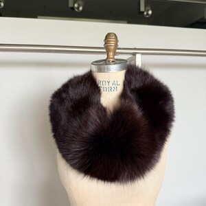 May include: A dark brown fur collar displayed on a mannequin. The collar is a full circle of soft, plush fur. The mannequin is a light beige color and has the words "ROYAL FORM" printed on it.