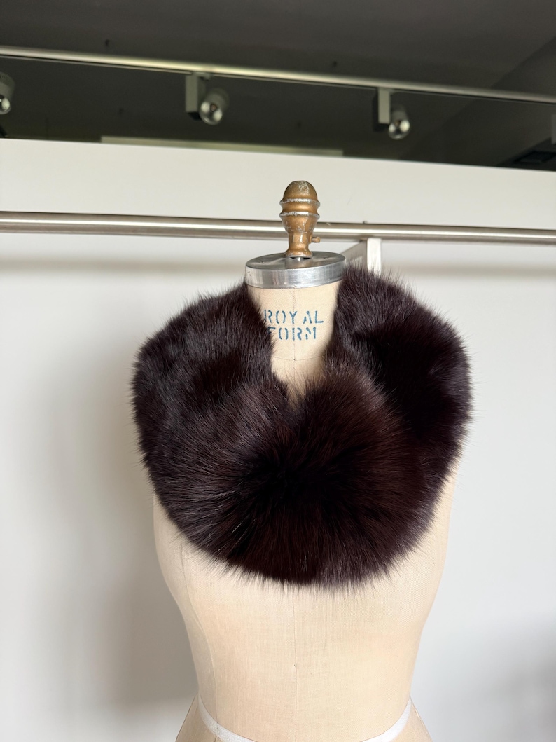 May include: A dark brown fur collar displayed on a mannequin. The collar is a full circle of soft, plush fur. The mannequin is a light beige color and has the words "ROYAL FORM" printed on it.