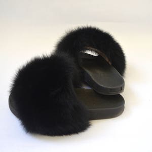 K&ouml;nnte beinhalten: Ein Paar schwarze, mit Fell gef&uuml;tterte Hausschuhe mit schwarzer Gummisohle.