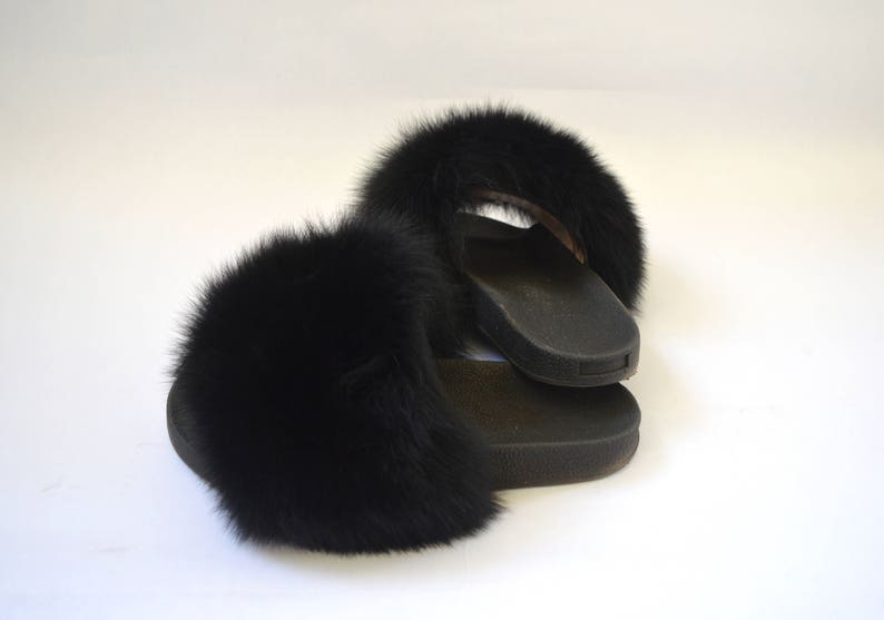 K&ouml;nnte beinhalten: Ein Paar schwarze, mit Fell gef&uuml;tterte Hausschuhe mit schwarzer Gummisohle.