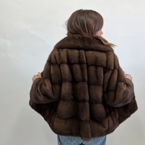 K&ouml;nnte beinhalten: Eine braune Pelzjacke mit einer kurzen L&auml;nge und einem Kragen. Die Jacke ist aus weichem, luxuri&ouml;sem Pelz gefertigt und hat einen klassischen, eleganten Stil.