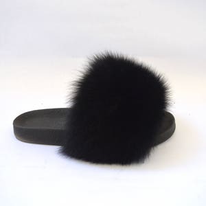 K&ouml;nnte beinhalten: Schwarze Fellsandalen mit einem gro&szlig;en, flauschigen Bommel oben.