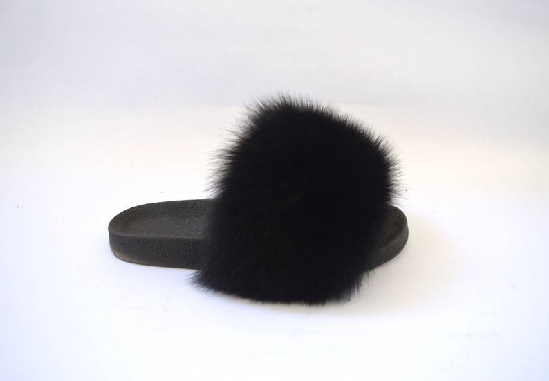 K&ouml;nnte beinhalten: Schwarze Fellsandalen mit einem gro&szlig;en, flauschigen Bommel oben.