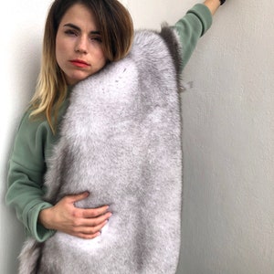 Puede incluir: Una mujer con un su&eacute;ter verde y una estola de piel blanca. La estola de piel est&aacute; drapeada sobre sus hombros y se mantiene en su lugar con sus manos.