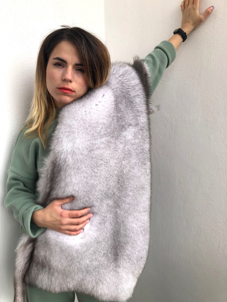 Puede incluir: Una mujer con un su&eacute;ter verde y una estola de piel blanca. La estola de piel est&aacute; drapeada sobre sus hombros y se mantiene en su lugar con sus manos.