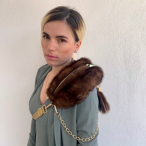 May include: A brown fur crossbody bag with a gold chain strap and a gold buckle. The bag has a zipper closure and a small fur tassel.