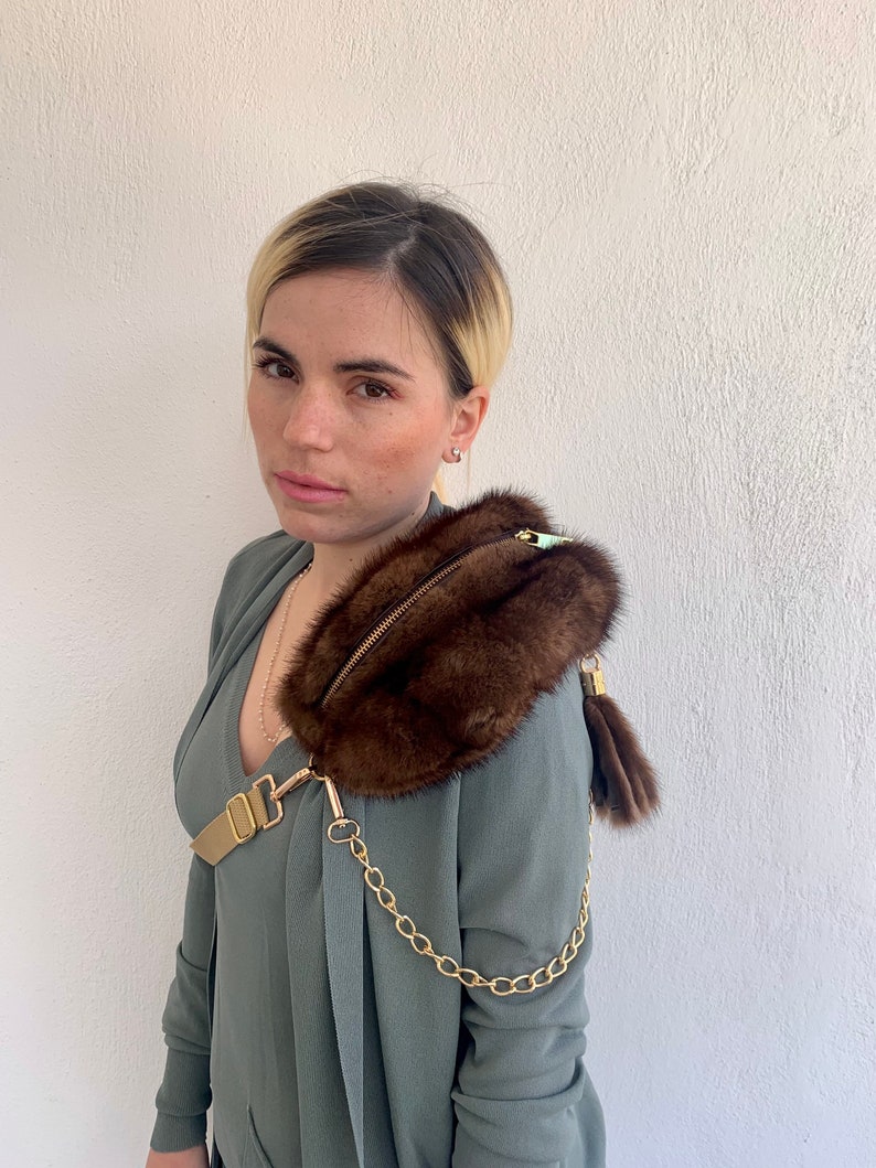 May include: A brown fur crossbody bag with a gold chain strap and a gold buckle. The bag has a zipper closure and a small fur tassel.