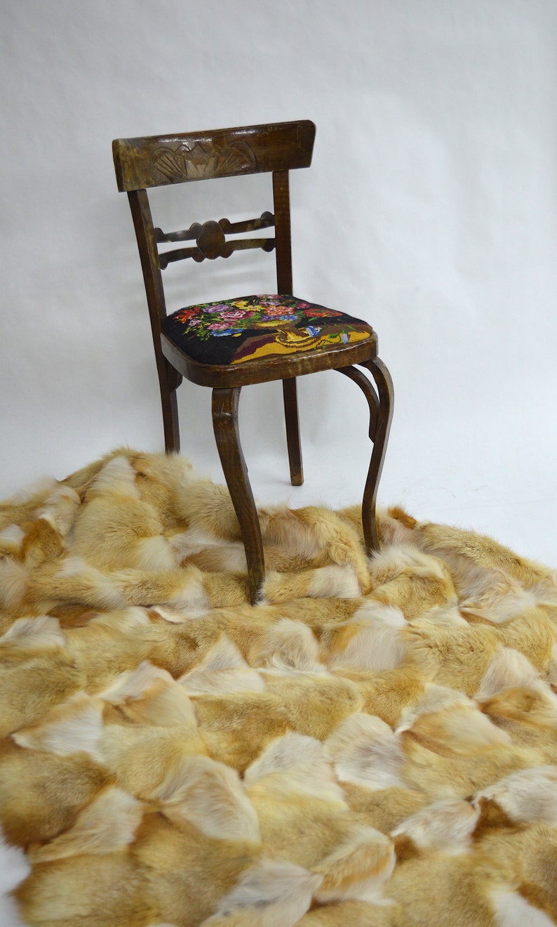 Op de afbeelding: Een houten stoel met een bloemmotief op de zitting staat op een pluche, lichtbruin vosbontkleed.