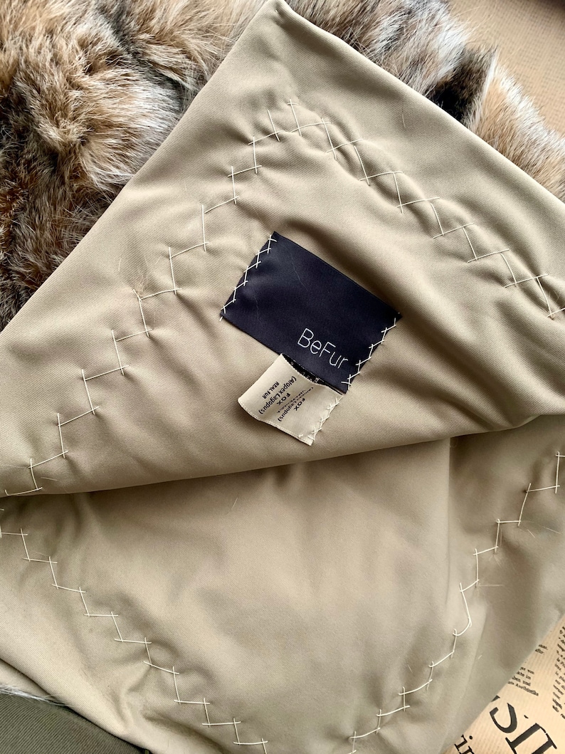 Pode incluir: Um forro de tecido bege com uma etiqueta preta que diz "BeFur" e uma etiqueta branca com o texto "Faux Fur (Angora turco) 100% Poli&eacute;ster Fabricado na China"