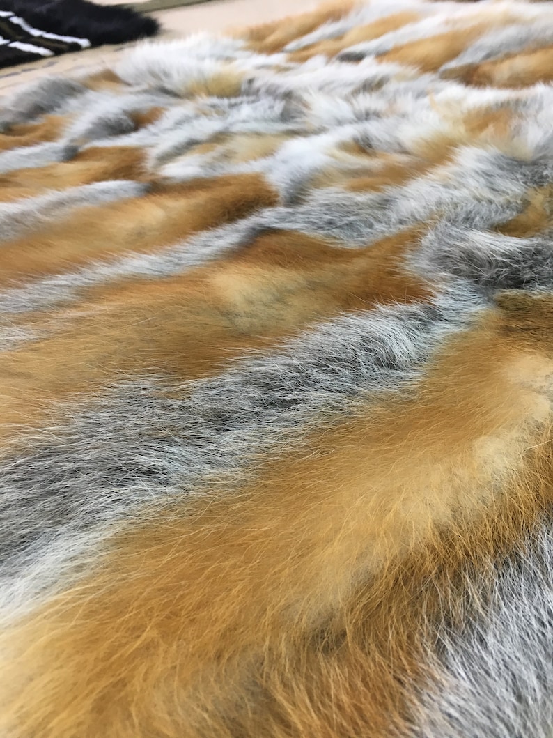 Pode incluir: Um close-up de um tapete de pele macio e felpudo com uma mistura de pele cinza, branca e laranja. A pele est&aacute; disposta em um padr&atilde;o ondulado, criando um visual luxuoso e texturizado.