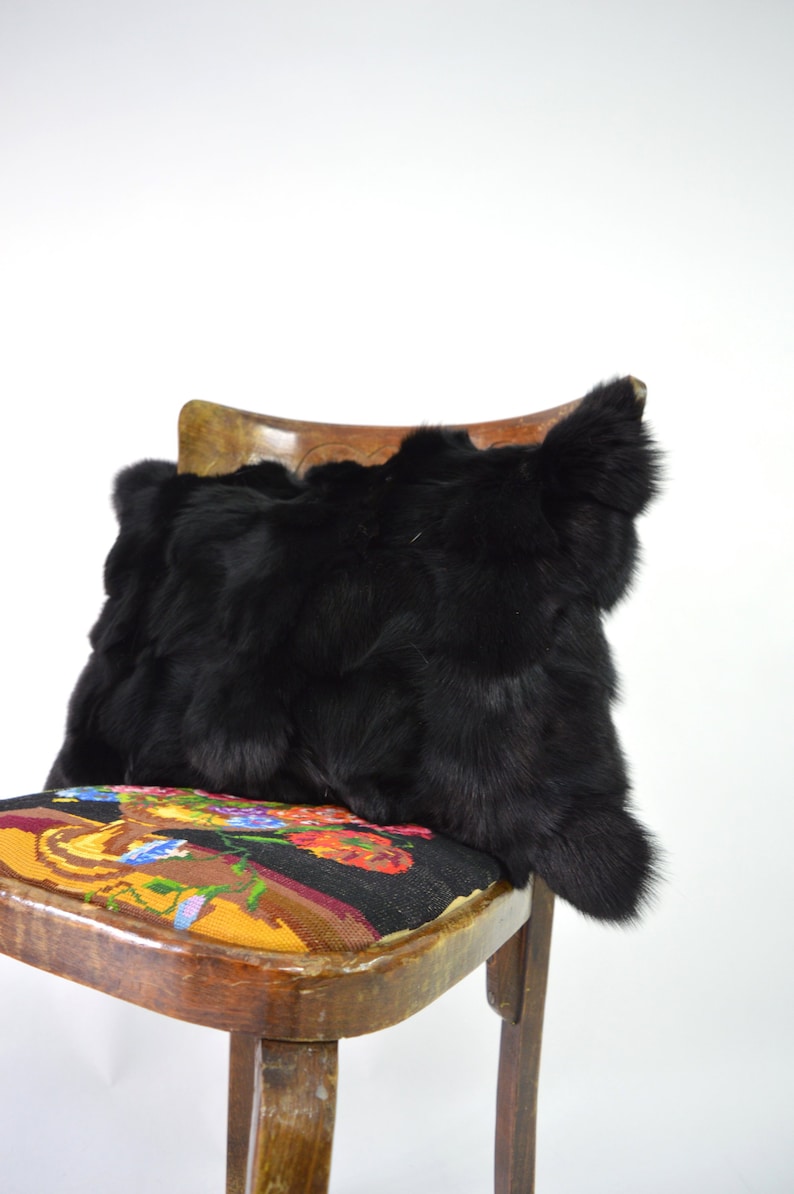 May include: A black fur pillow sits on a wooden chair with a colorful floral patterned seat cushion.