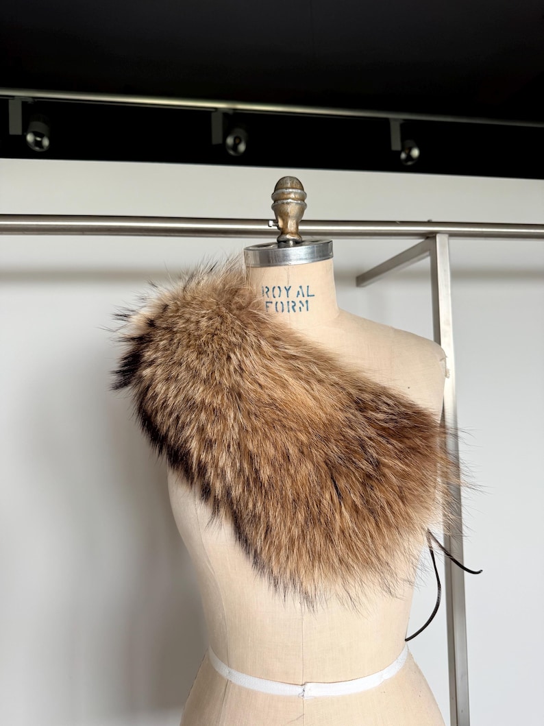 Op de afbeelding: Een bruine bontkraag met zwarte uiteinden, gedrapeerd over een mannequin. Het bont ziet er zacht en pluizig uit, met een mix van lichte en donkere bruintinten. De mannequin heeft de tekst "ROYAL FORM".