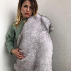 Puede incluir: Una mujer con un su&eacute;ter y pantalones verdes sostiene una estola de piel blanca alrededor del cuello. La piel es suave y esponjosa.