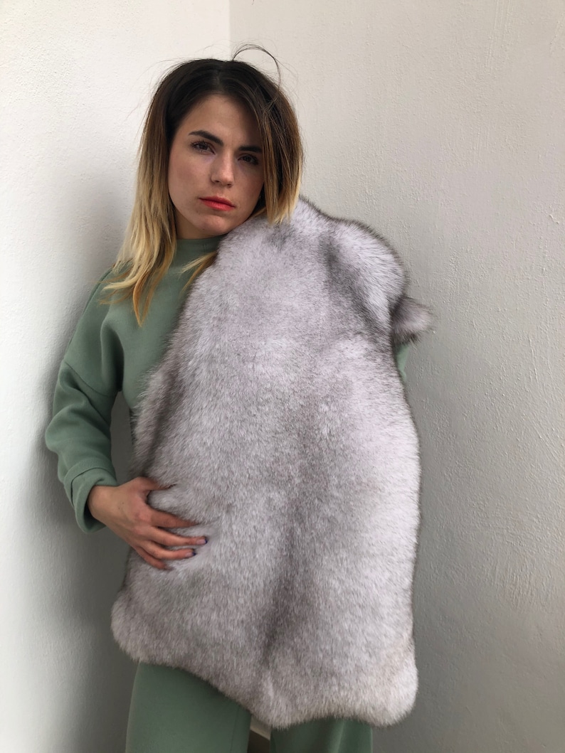 Puede incluir: Una mujer con un su&eacute;ter y pantalones verdes sostiene una estola de piel blanca alrededor del cuello. La piel es suave y esponjosa.