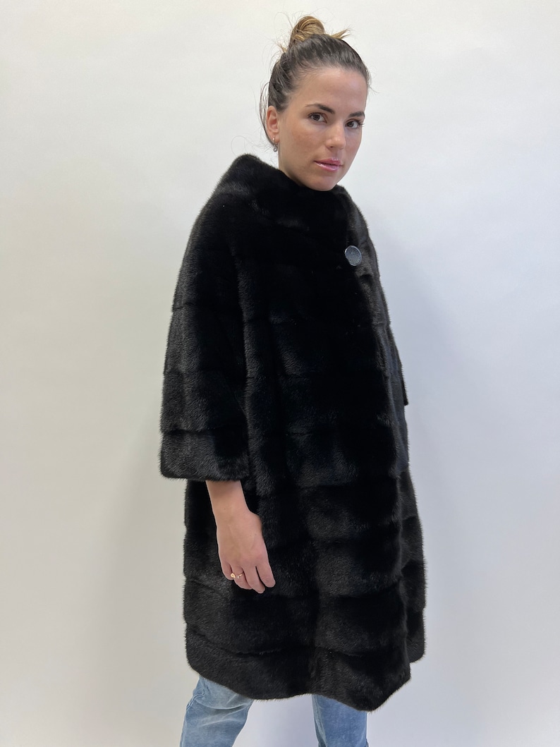 May include: A black fur coat with a single button fastening. The coat has a high collar and a straight silhouette.