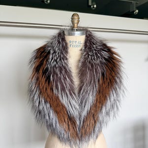 May include: A luxurious fur collar displayed on a mannequin. The collar features a mix of brown, silver, and reddish-brown fur. The mannequin is a light beige color, and the background is a neutral white.
