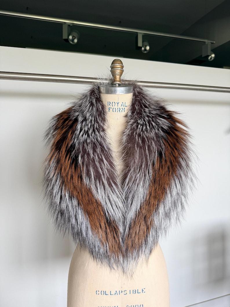 May include: A luxurious fur collar displayed on a mannequin. The collar features a mix of brown, silver, and reddish-brown fur. The mannequin is a light beige color, and the background is a neutral white.
