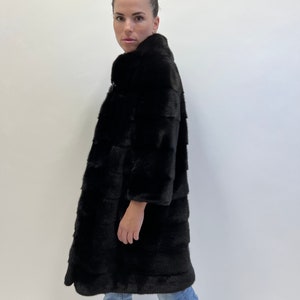 May include: A black fur coat with a high collar and a long, straight silhouette. The coat is made of soft, luxurious fur and has a sleek, modern design.