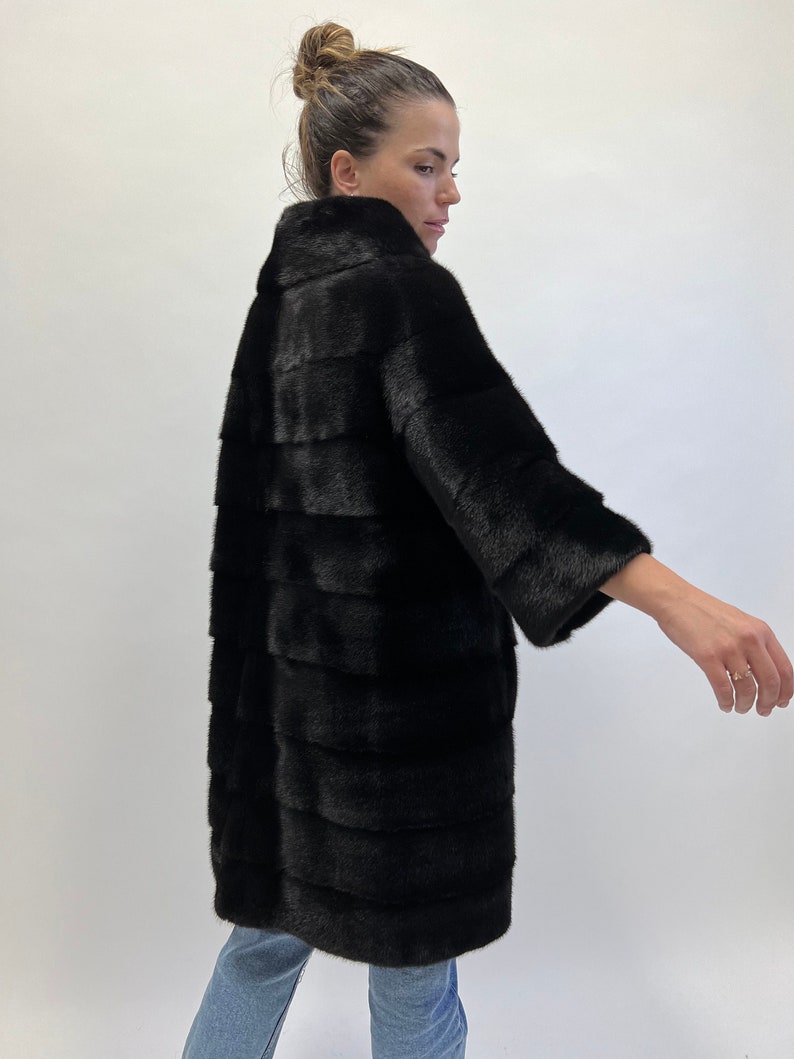 May include: A black fur coat with a high collar and long sleeves. The coat is made of a soft, luxurious fur and has a sleek, modern design.