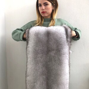 Puede incluir: Una mujer sostiene un trozo grande y rectangular de piel gris. La piel es suave y esponjosa, con un ligero brillo.