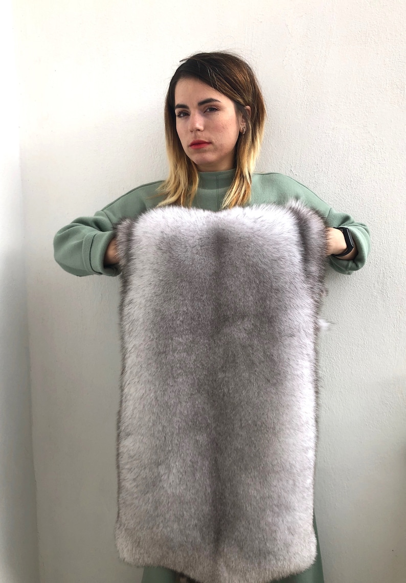 Puede incluir: Una mujer sostiene un trozo grande y rectangular de piel gris. La piel es suave y esponjosa, con un ligero brillo.