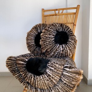 May include: Two round brown and white fur cushions with black fur centers on a bamboo chair.