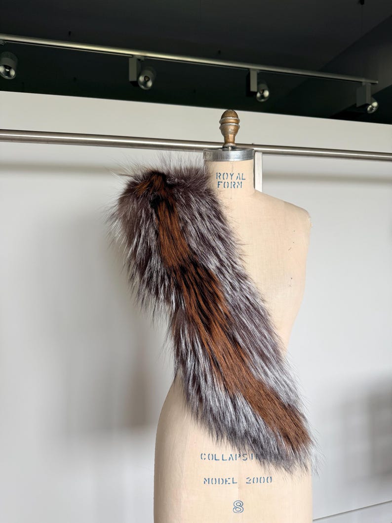 May include: A luxurious fur stole with a mix of brown, silver, and reddish-brown tones. The stole is draped over a mannequin, showcasing its texture and design. The fur appears soft and fluffy, perfect for adding a touch of elegance.