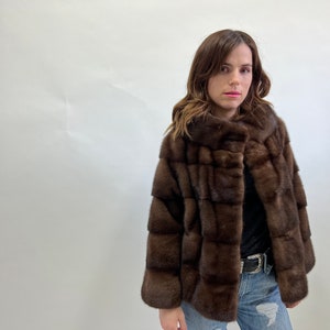 K&ouml;nnte beinhalten: Eine braune Pelzjacke mit hohem Kragen und Rei&szlig;verschluss. Die Jacke ist aus weichem, luxuri&ouml;sem Pelz gefertigt und hat ein elegantes, modernes Design.