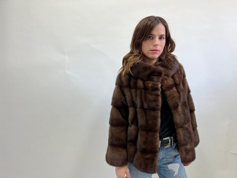 K&ouml;nnte beinhalten: Eine braune Pelzjacke mit hohem Kragen und Rei&szlig;verschluss. Die Jacke ist aus weichem, luxuri&ouml;sem Pelz gefertigt und hat ein elegantes, modernes Design.