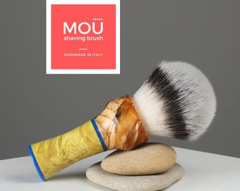 May include: A yellow and brown shaving brush with a blue band on the handle. The brush is made of natural boar bristles and is handmade in Italy. The brush is sitting on top of two gray stones.