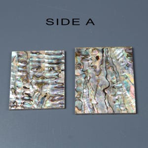 Op de afbeelding: Twee rechthoekige stukken van iriserende abalone-schelp, naast elkaar, met het label "ZIJDE A". De schelp heeft een natuurlijk, organisch patroon van bruin, zwart en wit.